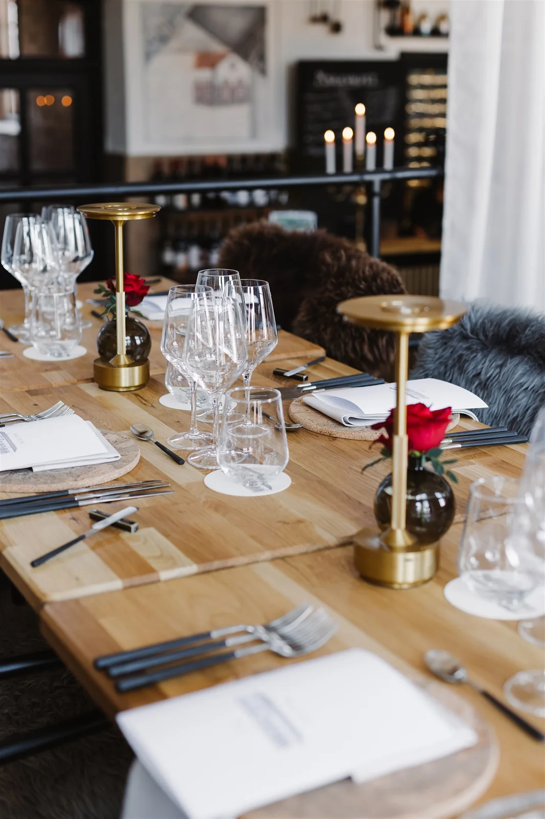 A table set with wine glasses, red roses and brass lamps in Kalcium’s dining room
